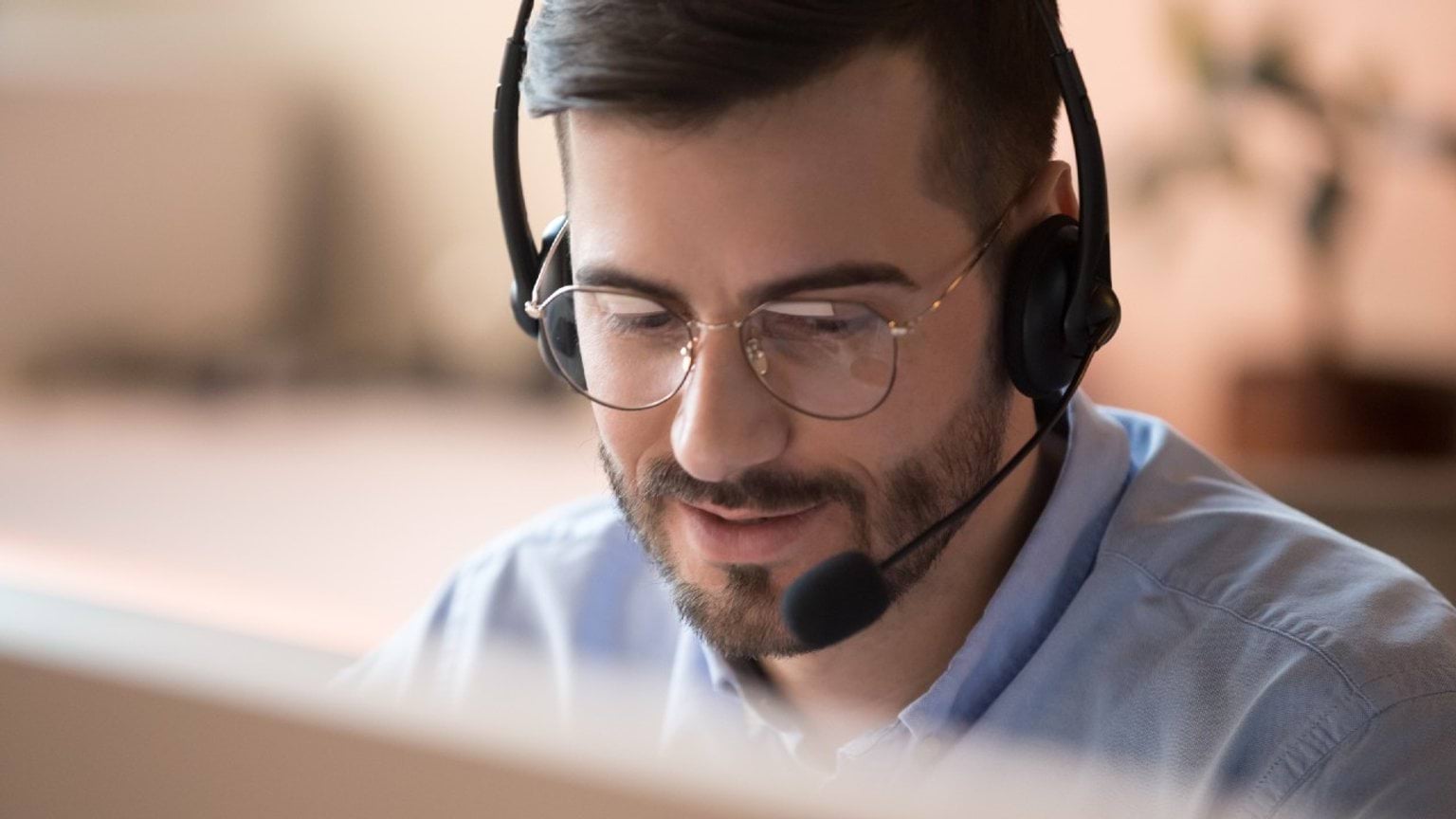 Man with glasses and headset, smiling while assisting customers.
